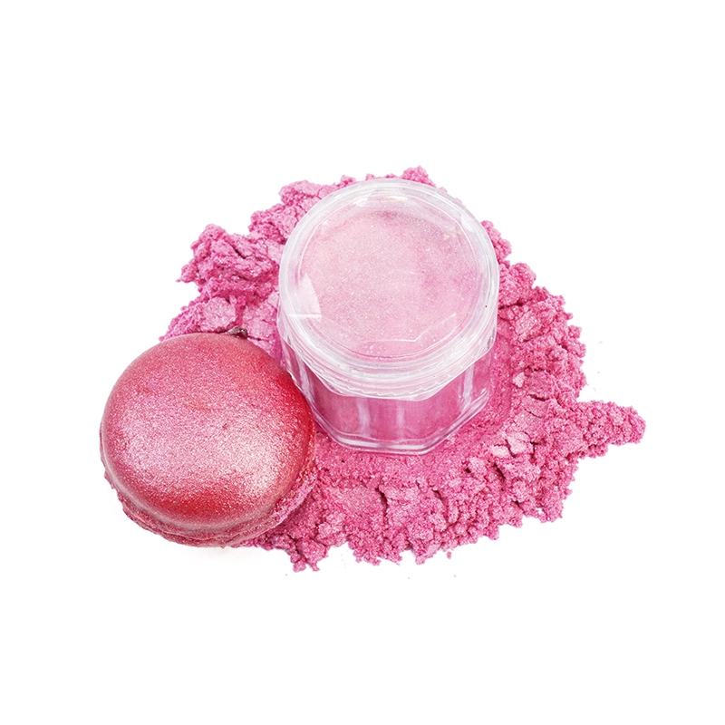 A pink macaron with a container of pink powder beside it, surrounded by pink powder scattered on a white background