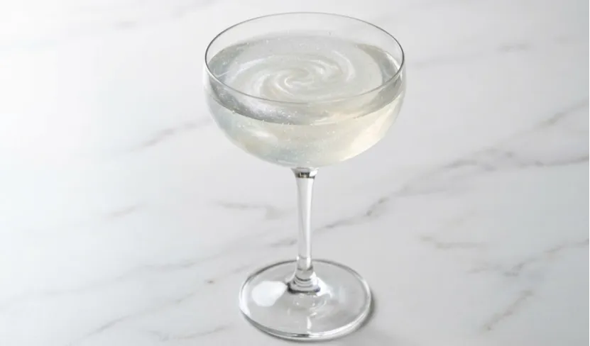 A cocktail in a coupe glass with a swirling pearlescent shimmer effect.