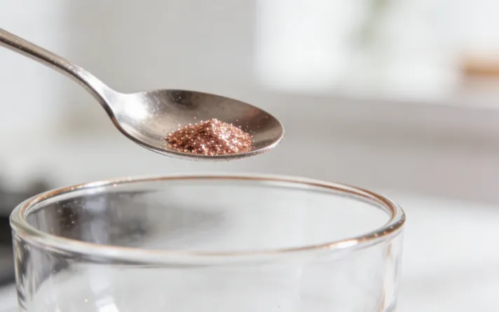 Spoon adding rose gold edible glitter to a glass.