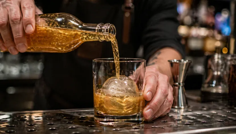 Bartender pouring a pre-batched gold shimmering cocktail over ice