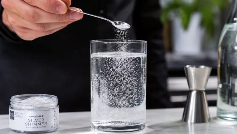 Adding silver edible shimmer powder to a glass of clear sparkling water