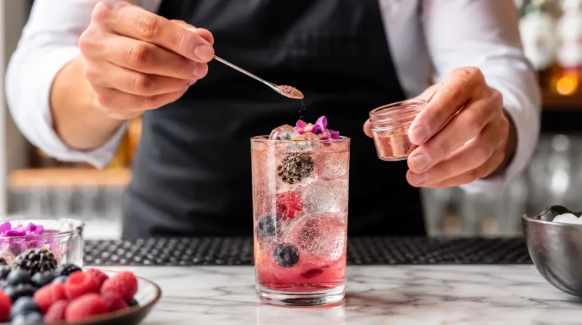 Bartender adding rose gold edible glitter to a fresh berry mocktail