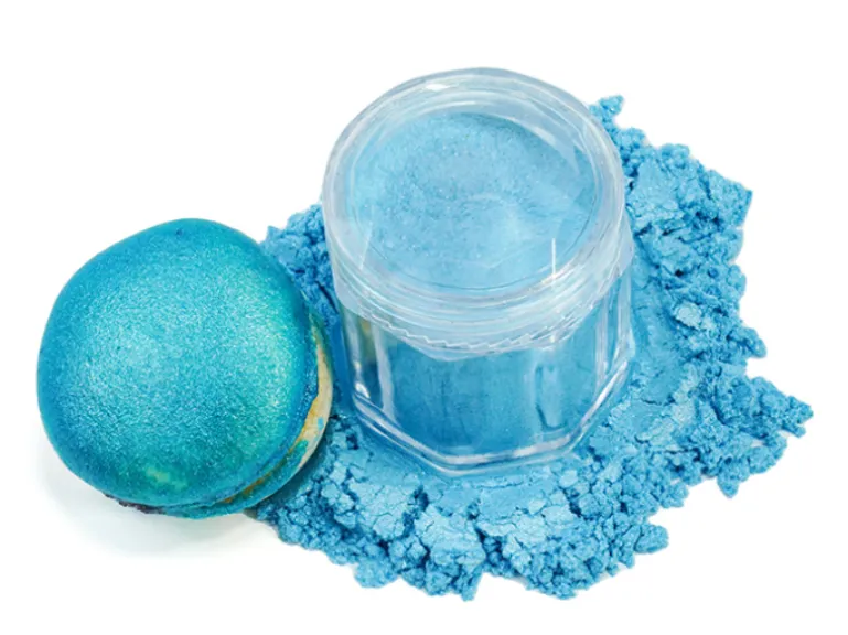 A blue macaron next to a jar of spilled blue luster dust