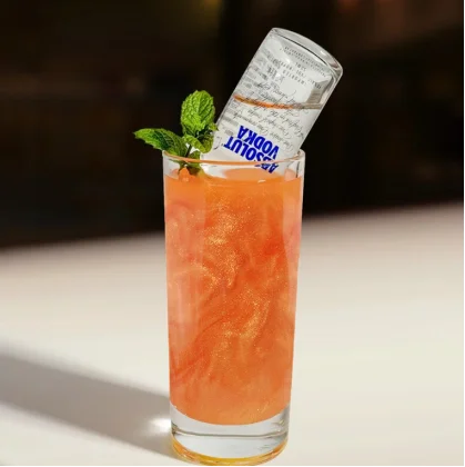Orange glitter cocktail with an upside-down mini vodka bottle